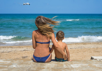 Mother with a young son look at the sea harbor. Family back sitting on a wood pontoon at seaside...
