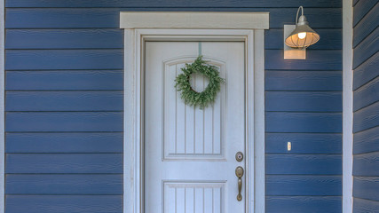 Wreath hanging on the white door of a blue home