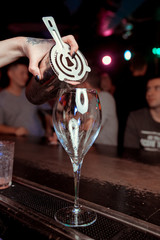 Barman pouring fresh alcoholic drink into the glasses with ice cubes on the bar counter