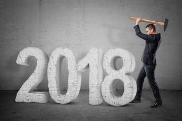 Businessman with a hammer breaking a stone '2018' sign on grey background