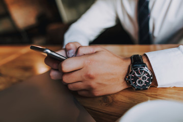Concept of success and well-being. Close up of smartphone in hands of young businessman checking...