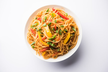Schezwan Noodles or vegetable Hakka Noodles or chow mein is a popular Indo-Chinese recipes, served in a bowl or plate with wooden chopsticks. selective focus