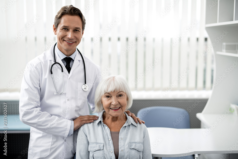 Wall mural emotional reliable doctor putting hands on the shoulders of his satisfied patient and smiling happil