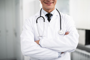 Cheerful enthusiastic doctor with stethoscope on his neck standing with his arms crossed and smiling happily