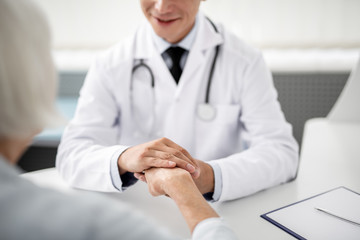 Kind smiling doctor sitting in front of his patient and gently touching her hand
