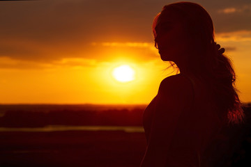 silhouette of a beautiful romantic girl at sunset , face profile of young woman with long hair in hot weather