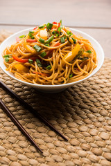 Schezwan Noodles or vegetable Hakka Noodles or chow mein is a popular Indo-Chinese recipes, served in a bowl or plate with wooden chopsticks. selective focus