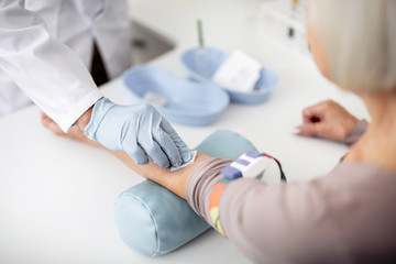 Careful doctor in rubber gloves cleaning the arm of his patient before the injection while standing...