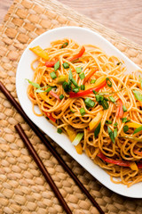 Schezwan Noodles or vegetable Hakka Noodles or chow mein is a popular Indo-Chinese recipes, served in a bowl or plate with wooden chopsticks. selective focus