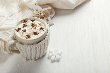 Fototapeta na wymiar A cup of hot winter drink with whipped cream and a dusting powder with an asterisk, white snowflakes and knitted scarf on a wooden table. Christmas concept in bright colors. Copy space.