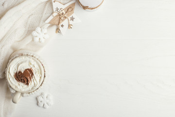 A cup of hot winter drink with whipped cream and a dusting powder with an asterisk, white snowflakes and knitted scarf on a wooden table. Christmas concept in bright colors. Copy space.