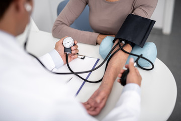 Female patient sitting at the table and general practitioner measuring her blood pressure