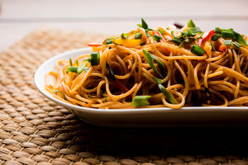 Schezwan Noodles or vegetable Hakka Noodles or chow mein is a popular Indo-Chinese recipes, served in a bowl or plate with wooden chopsticks. selective focus