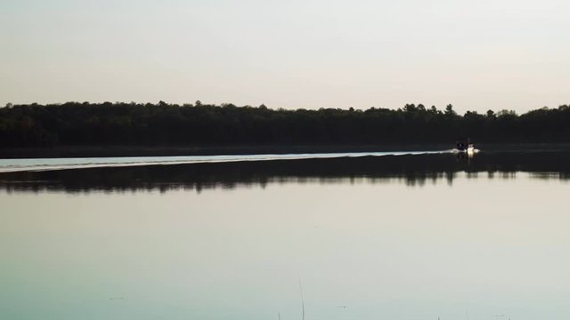 Boats crusing across beautiful scenic lake with woods near sunset