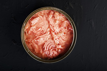 Tin with tuna slices on a black background. Canned fish. Semi finished
