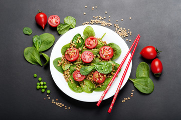 Salad of baby spinach leaves, green lentils, cherry tomatoes, olive oil and lemon juice in a bowl on a dark surface. A dietary dish. Vegetarian, vegan concept