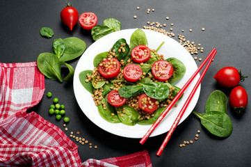 Salad of baby spinach leaves, green lentils, cherry tomatoes, olive oil and lemon juice in a bowl on a dark surface. A dietary dish. Vegetarian, vegan concept