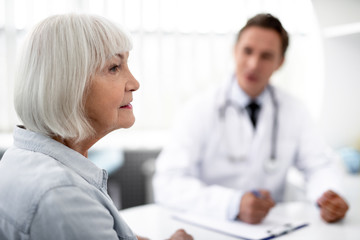 Obraz premium Close up of the face of aged woman thoughtfully looking into the distance with her practitioner sitting on the background