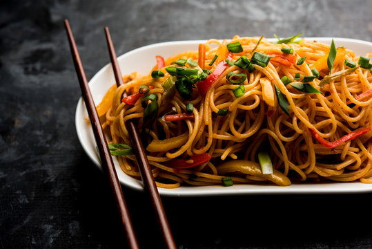 Schezwan Noodles or vegetable Hakka Noodles or chow mein is a popular Indo-Chinese recipes, served in a bowl or plate with wooden chopsticks. selective focus