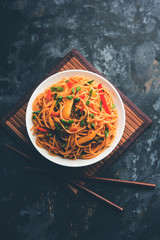 Schezwan Noodles or vegetable Hakka Noodles or chow mein is a popular Indo-Chinese recipes, served in a bowl or plate with wooden chopsticks. selective focus