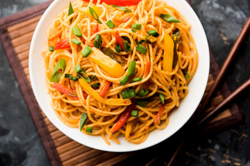 Schezwan Noodles or vegetable Hakka Noodles or chow mein is a popular Indo-Chinese recipes, served in a bowl or plate with wooden chopsticks. selective focus
