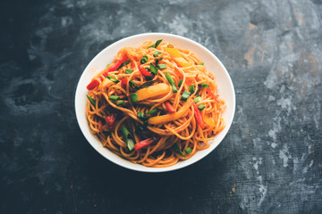 Schezwan Noodles or vegetable Hakka Noodles or chow mein is a popular Indo-Chinese recipes, served in a bowl or plate with wooden chopsticks. selective focus