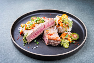 Traditional exotically tuna fish fillet with mango salsa and rice as closeup on a modern design black plate