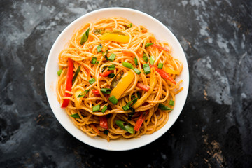 Schezwan Noodles or vegetable Hakka Noodles or chow mein is a popular Indo-Chinese recipes, served in a bowl or plate with wooden chopsticks. selective focus