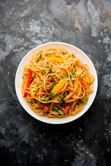 Schezwan Noodles or vegetable Hakka Noodles or chow mein is a popular Indo-Chinese recipes, served in a bowl or plate with wooden chopsticks. selective focus