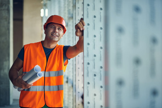 Confident professional builder holding his drawings and looking up while standing alone and smiling