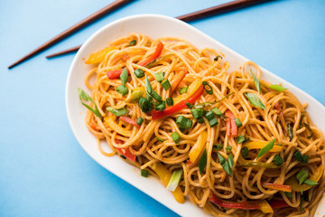 Schezwan Noodles or vegetable Hakka Noodles or chow mein is a popular Indo-Chinese recipes, served in a bowl or plate with wooden chopsticks. selective focus