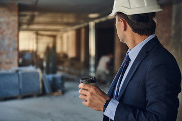 Waist up portrait of architect standing on construction site and holding coffee in his hands. Copy...