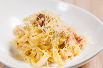 Pasta with meat and cheese in white plate on light wooden table in a restaurant