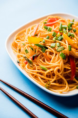 Schezwan Noodles or vegetable Hakka Noodles or chow mein is a popular Indo-Chinese recipes, served in a bowl or plate with wooden chopsticks. selective focus