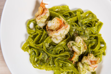 Green pasta with shrimps and cheese in white plate on light wooden table in a restaurant