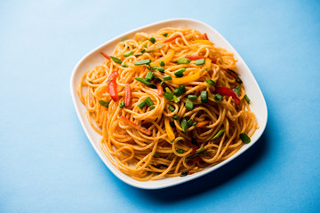 Schezwan Noodles or vegetable Hakka Noodles or chow mein is a popular Indo-Chinese recipes, served in a bowl or plate with wooden chopsticks. selective focus