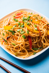 Schezwan Noodles or vegetable Hakka Noodles or chow mein is a popular Indo-Chinese recipes, served in a bowl or plate with wooden chopsticks. selective focus