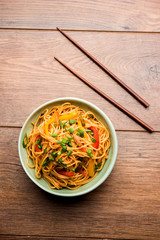 Schezwan Noodles or vegetable Hakka Noodles or chow mein is a popular Indo-Chinese recipes, served in a bowl or plate with wooden chopsticks. selective focus