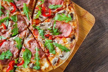Pizza with Mozzarella cheese, mushrooms, ham, tomato sauce, salami, pepper, Spices and Fresh arugula. Italian pizza on wooden table background