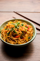 Schezwan Noodles or vegetable Hakka Noodles or chow mein is a popular Indo-Chinese recipes, served in a bowl or plate with wooden chopsticks. selective focus