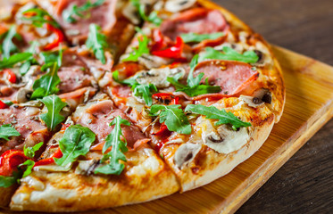 Pizza with Mozzarella cheese, mushrooms, ham, tomato sauce, salami, pepper, Spices and Fresh arugula. Italian pizza on wooden table background