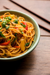 Schezwan Noodles or vegetable Hakka Noodles or chow mein is a popular Indo-Chinese recipes, served in a bowl or plate with wooden chopsticks. selective focus
