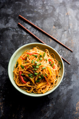 Schezwan Noodles or vegetable Hakka Noodles or chow mein is a popular Indo-Chinese recipes, served in a bowl or plate with wooden chopsticks. selective focus
