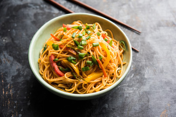 Schezwan Noodles or vegetable Hakka Noodles or chow mein is a popular Indo-Chinese recipes, served in a bowl or plate with wooden chopsticks. selective focus
