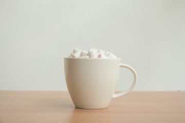 Fototapeta na wymiar Fluffy white marshmallow in white cup on wooden table,Hot chocolate,Minimal.