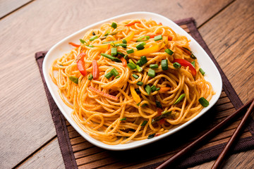 Schezwan Noodles or vegetable Hakka Noodles or chow mein is a popular Indo-Chinese recipes, served in a bowl or plate with wooden chopsticks. selective focus