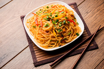 Schezwan Noodles or vegetable Hakka Noodles or chow mein is a popular Indo-Chinese recipes, served in a bowl or plate with wooden chopsticks. selective focus