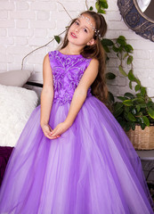 little girl in violet shiny dress with bow. kid christmas costume. young girl princess in white room is standing in violet fancy skirt and smiling cute