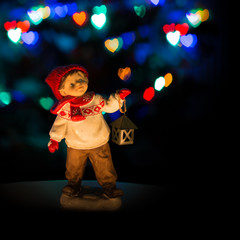 Boy ceramic figurine with lantern in winter on christmas hart bokeh light background