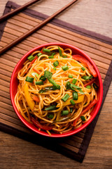 Schezwan Noodles or vegetable Hakka Noodles or chow mein is a popular Indo-Chinese recipes, served in a bowl or plate with wooden chopsticks. selective focus